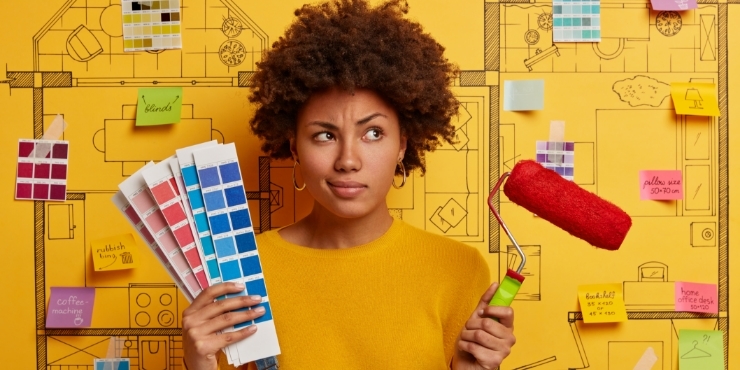 a black woman in front of a large yellow blueprint holds paint samples and a paint roller